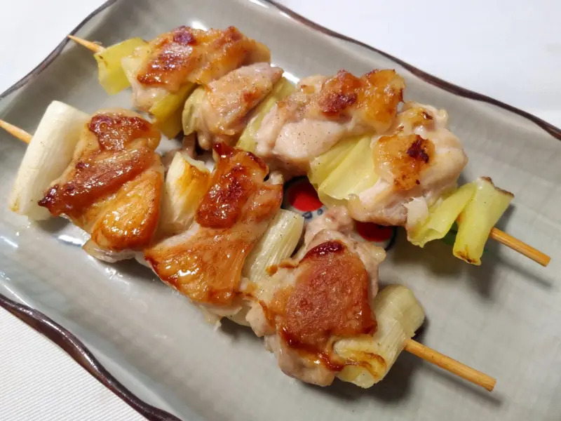 A skewer with chicken and green onion pieces
