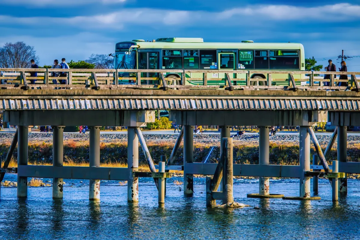 A Kyoto City bus crossing Togetsukyo Bridge in Arashiyama with mountains in the background.