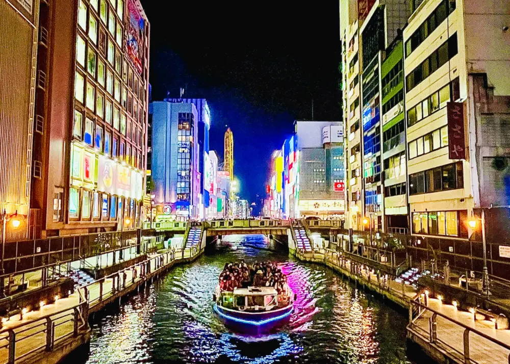 A Dotonbori Canal cruise boat passing under illuminated bridges in Osaka.