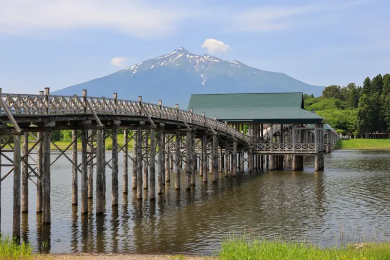 A wooden arch bridge reflecting in a calm lake.
