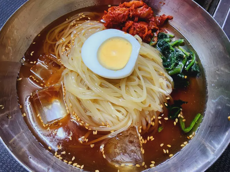 A bowl of Morioka Reimen with chilled broth, kimchi, and fresh toppings