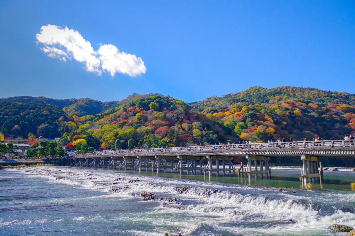 Togetsukyo Bridge in Arashiyama, Kyoto, with vibrant autumn colors in the background.