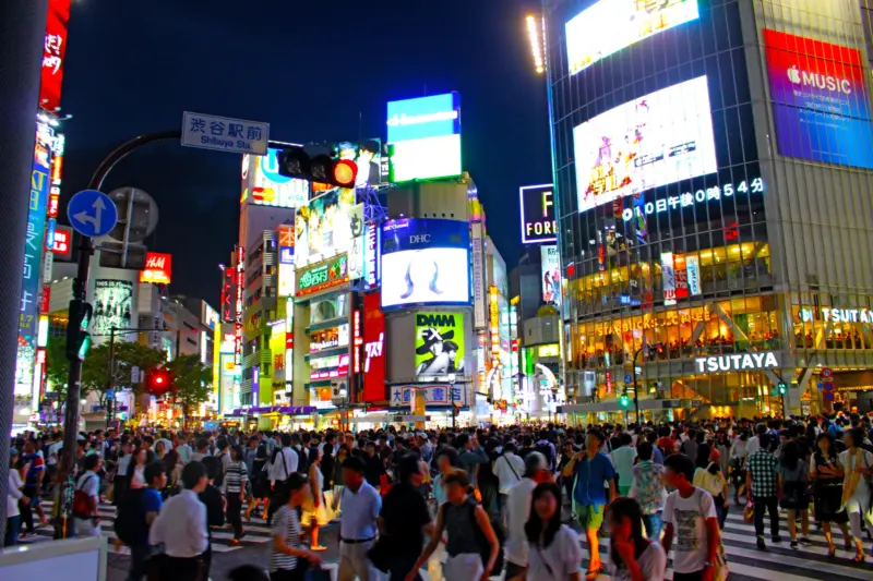 Shibuya Crossing in Tokyo, lit by neon signs and bustling with people.