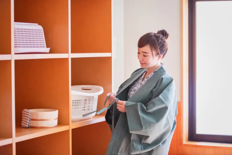 A woman undressing in the onsen changing room, preparing for her bath.
