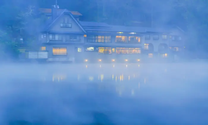 The serene Lake Kinrin with mist rising in the morning, surrounded by lush greenery in Yufuin