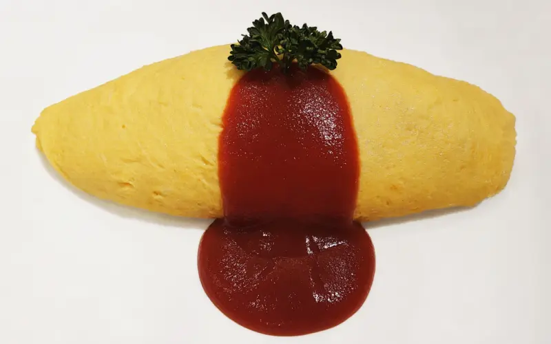 A plate of omurice topped with ketchup and served with a side salad.
