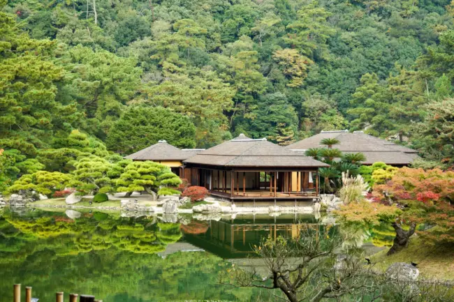A serene pond with a traditional teahouse surrounded by seasonal flowers in Ritsurin Garden, Kagawa