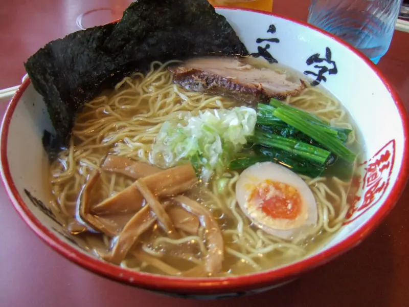 A bowl of clear shio ramen topped with chashu pork, bamboo shoots, and green onions.