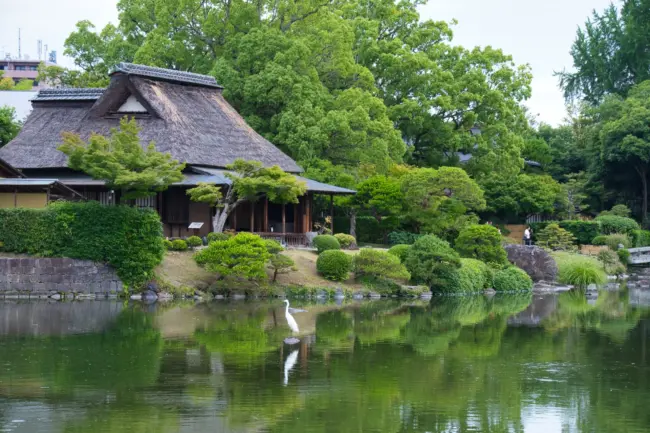 A serene pond and traditional teahouse surrounded by greenery at Suizenji Jojuen Garden in Kumamoto