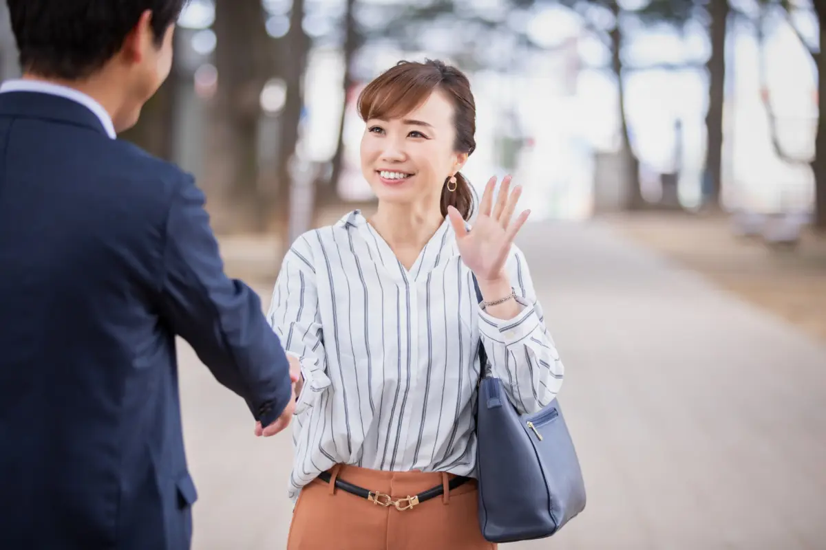 A woman raising her hand to greet with a friendly smile.