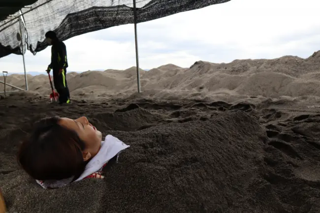 A visitor relaxing in a natural sand bath along the coast in Ibusuki, Kagoshima.