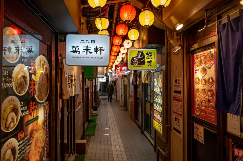 Brightly lit entrance to Sapporo Ramen Alley with signs of various ramen shops.