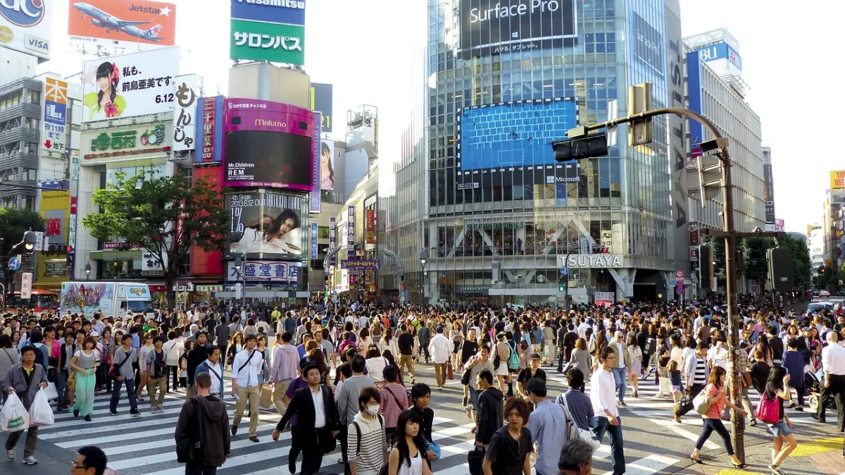 A large crowd of people walking through the Shibuya Scramble Crossing.