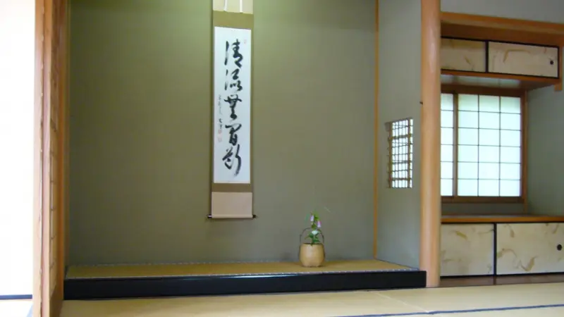 A decorative tokonoma with a hanging scroll and a flower arrangement in a tatami room.