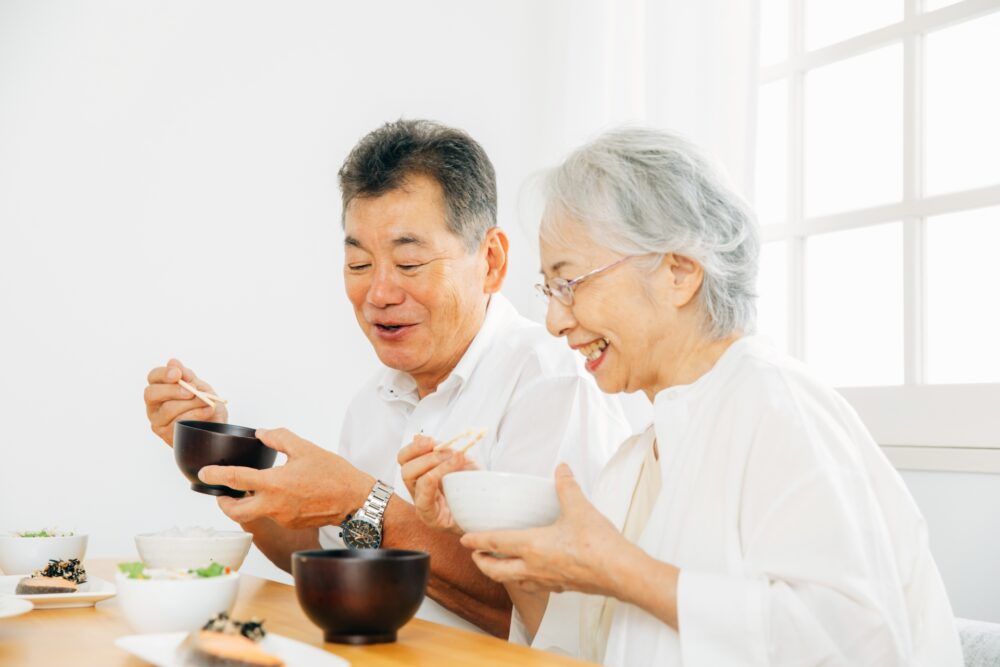 A Japanese person holding a rice bowl while using chopsticks at a traditional meal.